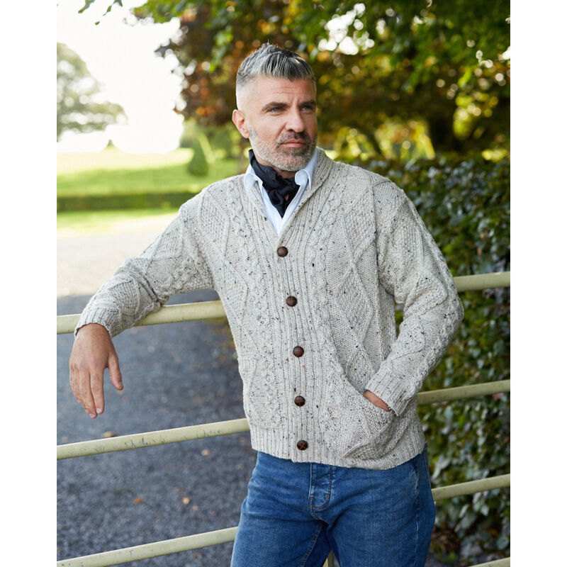 Man leaning against a metal gate in an outdoor garden wearing an oatmeal coloured aran knitted cardigan